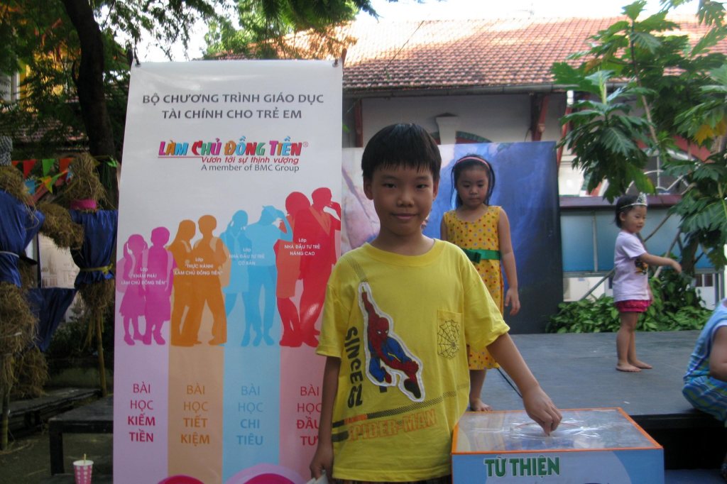 Cậu bé bỏ tiền vào hộp từ thiện cạnh băng rôn 5 bài học Làm Chủ Đồng Tiền